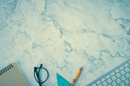 Modern Clean Flat Lay or Top View Office Desk or Office Table and Office Supplies as Computer Keyboard,Pen,Glasses,Spiral Notebook,Triangle Ruler on Marble Minimalist Background in Vintage Toneの写真素材