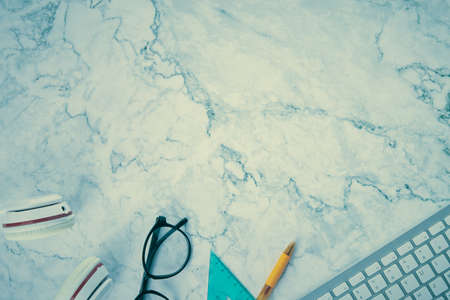 Modern Clean Flat Lay or Top View Office Desk or Office Table and Office Supplies as Computer Keyboard,Pen,Glasses,Headphone,Triangle Ruler on Marble Minimalist Background in Vintage Toneの写真素材