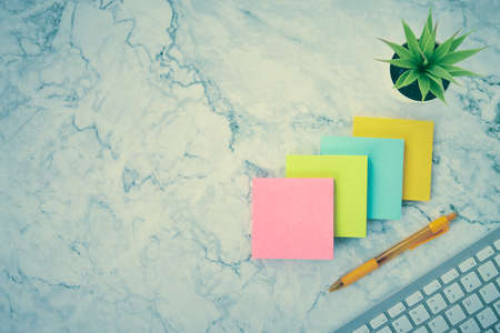 Four Color Stick Note or Notepad and Computer Keyboard and Office Plant and Pen on Modern Clean Marble Office Desk or Office Table Background in Vintage Toneの写真素材
