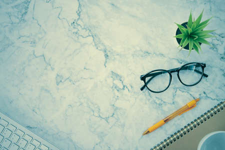 Modern Clean Flat Lay or Top View Office Desk or Office Table and Office Supplies as Computer Keyboard,Pen,Spiral Notebook,Office Plants,Glasses,Coffee Cup on Marble Minimalist Background in Vintage Toneの写真素材