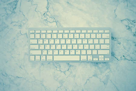 Modern Clean White Computer Keyboard on Flat Lay or Top View Office Desk or Office Table on Marble Minimalist Background in Vintage Toneの写真素材