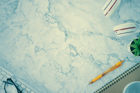Modern Clean Flat Lay or Top View Office Desk or Office Table and Office Supplies as Computer Keyboard,Pen,Spiral Notebook,Office Plants,Glasses,Headphone,Coffee Cup on Marble Minimalist Background in Vintage Toneの写真素材