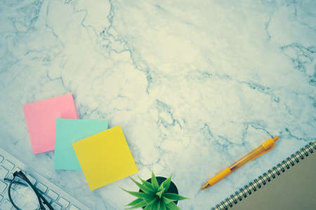 Modern Clean Flat Lay or Top View Office Desk or Office Table and Office Supplies as Stick Note or Notepad,Computer Keyboard,Pen,Spiral Notebook,Office Plants,Glasses on Marble Minimalist Background in Vintage Toneの写真素材