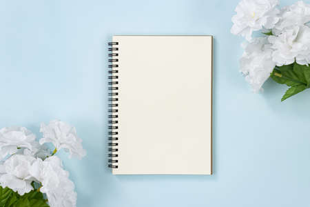 Spiral Notebook or Spring Notebook in Unlined Type and White Flowers at Top Right Corner and Bottom Left Corner on Blue Pastel Minimalist Backgroundの写真素材