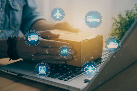 Hand of Casual Businessman or Entrepreneur Catch Parcel or Box on Laptop and Blue Logistic or Transportation Sign. SME Online Business and E-commerce Concept for Work at Home in Vintage Toneの写真素材