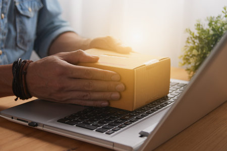 Hand of Casual Businessman or Entrepreneur Catch Parcel or Box on Laptop on Wood Table with Office Plants. SME Online Business and E-commerce Concept for Work at Homeの写真素材