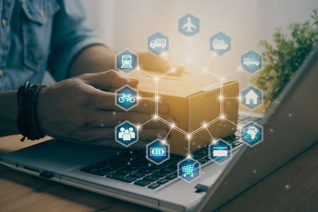 Hand of Casual Businessman or Entrepreneur Catch Parcel or Box on Laptop and Blue Hexagonal Logistic or Transportation Icon. SME Online Business and E-commerce Concept for Work at Home in Vintage Toneの写真素材