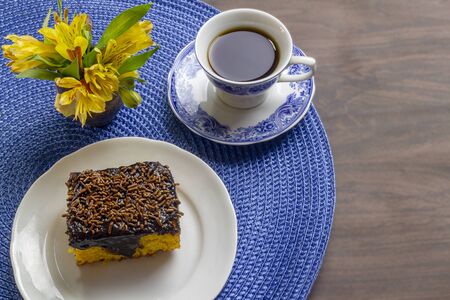 Carrot cake with chocolate icing and cup of coffee on wooden table decorated with a yellow flower.の写真素材