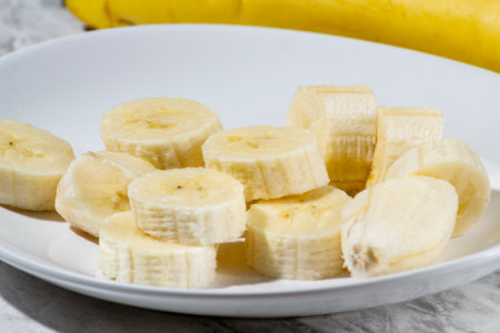 A bunch of bananas and a sliced banana on a plate on a table.の写真素材
