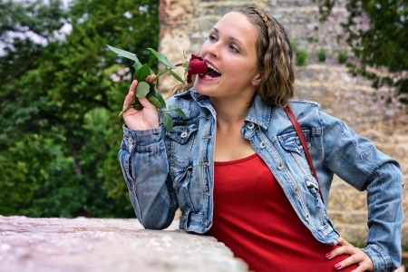Beautiful young woman standing near of a wall and biting a roseの写真素材
