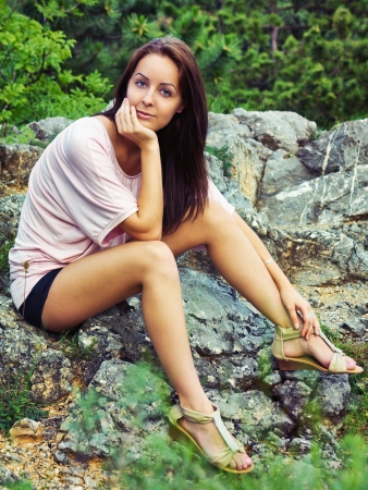 Beautiful young woman sitting on a rock and looking at the cameraの写真素材