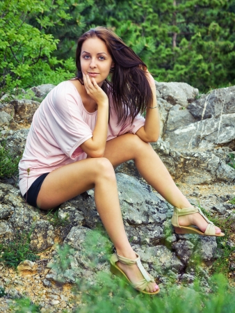 Beautiful young woman sitting on a rock and looking at the cameraの写真素材