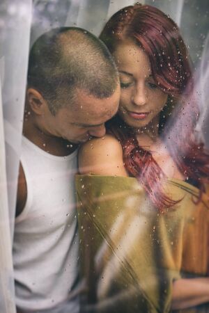 Attractive Couple behind the window in the rainy day. Focus on water drops are, the couple also Slightly blurredの写真素材