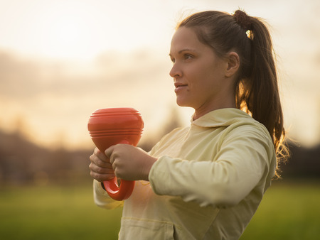 Outdoor photo of the young woman from training with kettlebells, sunset in the backgroundの写真素材