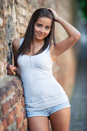 Beautiful young woman smiling and standing on the brick wallの写真素材