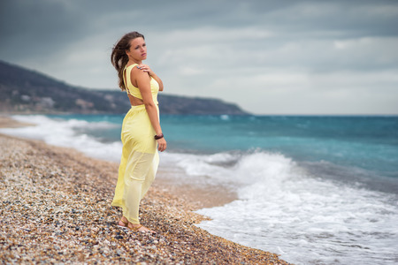 Lonely young woman standing at the coastline in the stormy weatherの写真素材