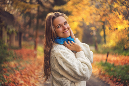 Young women smiling to the camera, beautiful autumn road in the background. This image was created with rare and special lens with unique vintage "swirly bokeh"の写真素材