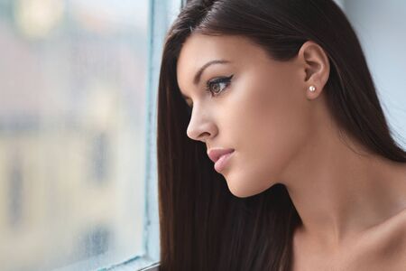 Beautiful young woman looking out the windowの写真素材