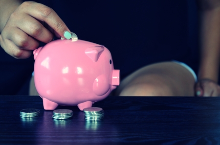 Woman is putting a coin into a pink piggy bank.の写真素材