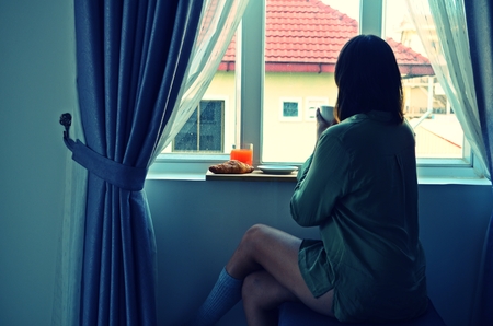 Beautiful woman by the window, she is holding a cup of coffee in the morning.の写真素材