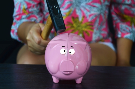 Woman is going to break a piggy bank with a hammer.の写真素材
