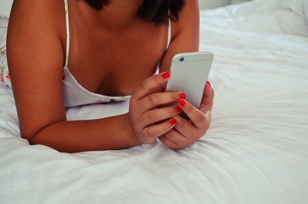Casual young woman is holding a phone on the bed.の写真素材