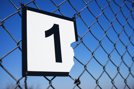 Broken sign attached to fence against sky background. Number oneの写真素材