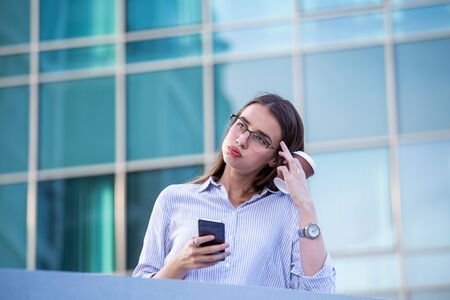 Business woman recieving bad news on smartphone and drinking coffee from disposable paper cup in the street with office buildings in the background.の写真素材