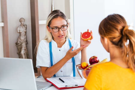 Portrait of young smiling female nutritionist in the consultation room. Making diet plan. Young woman visiting nutritionist in weight loss clinicの写真素材