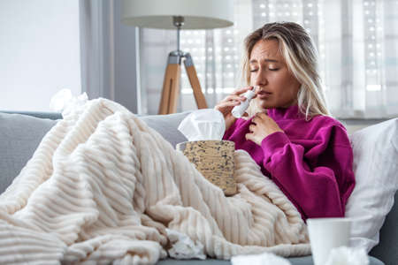 Woman is having flu and she is using nasal spray to help herself. Woman using nasal spray. Nasal spray to help a cold. Sick with a rhinitis woman dripping nose. Woman applies nasal sprayの写真素材