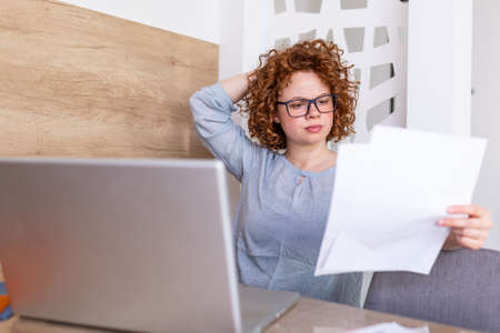 Upset business woman looking at documents and paperwork she is sitting at the table at workstation....