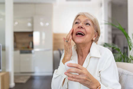 Perfect, pretty, woman applying eye cream, holding jar of cosmetic product. Portrait of senior woman applying anti-aging creamの写真素材