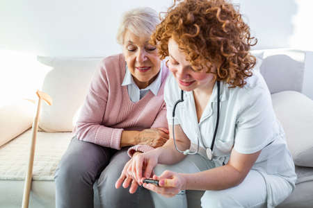 Nurse measuring blood sugar of senior woman at home. Young nurse measuring blood sugar of elderly woman at home. Doctor checking elderly woman's blood sugar - diabetes and glicemia conceptの素材 [FY310188409569]