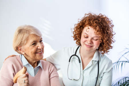 Happy patient is holding caregiver for a hand while spending time together. Elderly woman in nursing...
