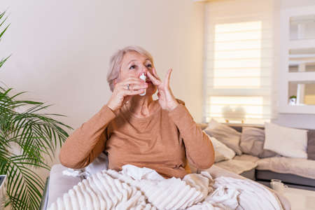 Senior Woman is having allergies and she is using nasal spray to help herself. Elder woman using nasal spray. Nasal spray to help a cold. Sick with a rhinitis woman dripping nose applies nasal sprayの写真素材