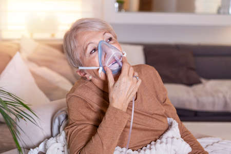 Sick elderly woman making inhalation, medicine is the best medicine. Ill senior woman wearing an oxygen mask and undergoing treatment. Senior woman with an inhalerの写真素材