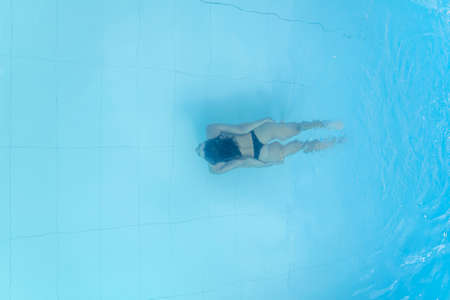 Drone view on young woman diving in blue swimming poolの写真素材