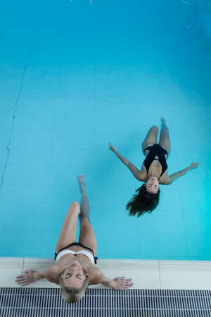 Rearview shot of two young women relaxing in the pool at a spaの写真素材