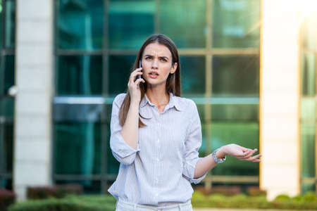 Businesswoman in formal wear having trouble with contracts talking on the phone and holding...