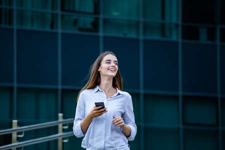 Happy smiling business woman talking on mobile smartphone in the street with office buildings in the...