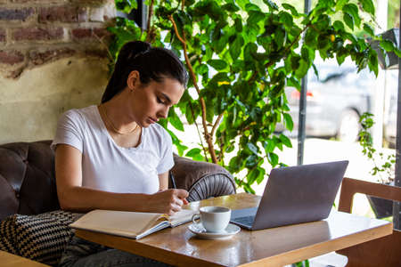 Young woman with coffee cup and laptop at coffe shop. Woman taking a break. Enjoying work from...