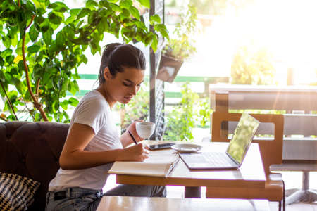 Young female with cute smile sitting with portable net-book in modern coffee shop interior during...
