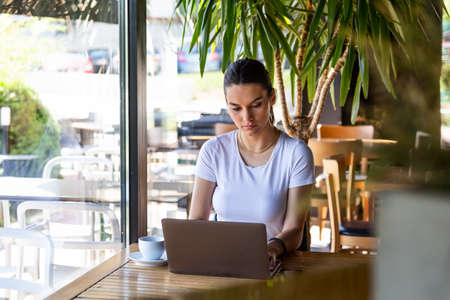 Young beautiful girl sitting at a table in a cafe by the window, drinking cappuccino coffee....