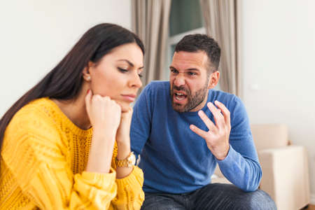 Young sad afraid woman and her violent screaming man. Young couple fighting at home, boyfriend shouting at girlfriend. Stressed out couple having problems. Divorce concept.の写真素材