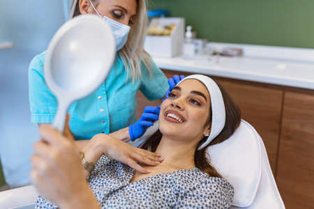 Concept of relaxation and body care. Top angle portrait of female therapist making anti-age massage of forehead wrinkles to young woman in spa salonの写真素材