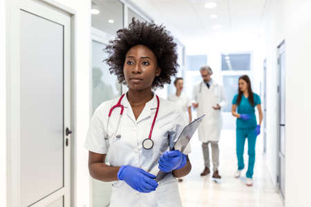 Serious African American female doctor walking with patient's test results before meeting with the patient. The doctor is in a hospital hallway.の写真素材