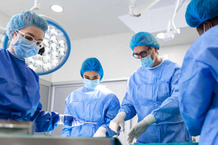 Portrait of team of multiethnic surgeons at work in a operation theatre. Several doctors surrounding patient on operation table during their work. Team surgeons at work in operating room.の写真素材