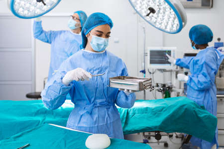Female surgeon in surgical uniform taking surgical instruments at operating room. Young woman doctor in hospital operation theaterの写真素材