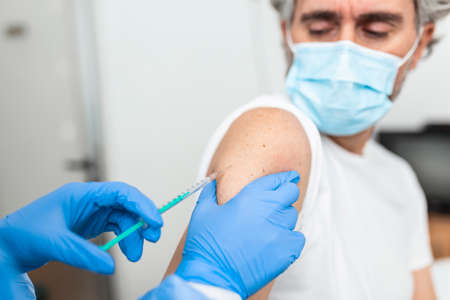 Vaccination, immunization, disease prevention concept. Patient getting Covid-19 vaccine at doctor's office. Cropped shot of professional nurse in medical face mask giving flu injection to senior manの写真素材