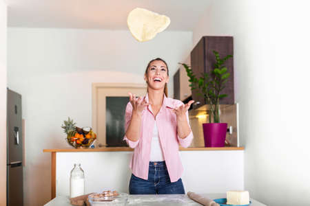 young woman tossing pizza dough in the air. Young woman knead dough at kitchen, homemade bakery...